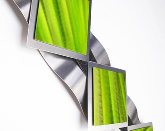 May include: Modern metal wall art featuring a series of square frames with vibrant green abstract art. The frames are set against a wavy, brushed metal background with black accents, creating a contemporary design.