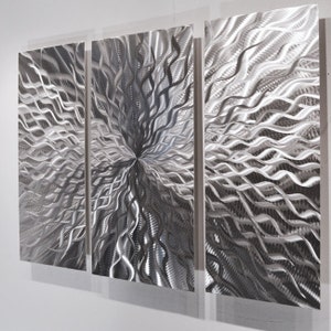 May include: A three-piece metal wall art set with a silver finish. The abstract design features swirling, wavy lines that create a dynamic and modern look.