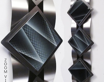 Puede incluir: Arte de pared abstracto con tres paneles en forma de diamante negro y plateado con un diseño geométrico texturizado. Los paneles están montados sobre un fondo ondulado de metal plateado.