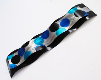 May include: Abstract metal wall art with a wavy design. The art features black, silver, and blue colors with a polka dot pattern.