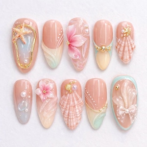 Peut inclure: Dix faux ongles en forme d'amande sur le thème de la plage. Chaque ongle présente un design différent, avec une étoile de mer, des fleurs, des coquillages et des perles, dans des tons de rose, d'or et de bleu. Les ongles sont décorés d'éléments 3D.