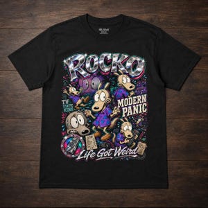 May include: Black t-shirt featuring a colorful graphic of Rocko and other characters from the animated series. The design includes the word "ROCKO" in a shiny, metallic font, along with the phrases "TV Static King", "Modern Panic", and "Life Got Weird".