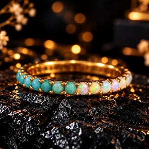 Könnte beinhalten: Ein goldener Ring mit einer Reihe abwechselnder runder Edelsteine, wobei eine Hälfte mit undurchsichtigen türkisfarbenen Steinen und die andere Hälfte mit schillernden weißen Opalen besetzt ist, was einen Farbverlauf erzeugt.