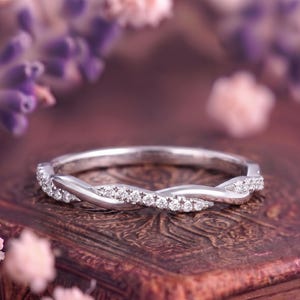 Könnte beinhalten: Ein Ring aus silberfarbenem Metall mit einem gedrehten Banddesign. Ein Strang der Drehung ist glatt und poliert, während der andere Strang mit einer Reihe kleiner, klarer, rund geschliffener Steine besetzt ist, die entlang der Vorderseite verlaufen.