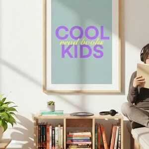 Könnte beinhalten: Gerahmtes Poster mit den Worten "COOL read books KIDS" in lila und gelben Buchstaben. Das Poster hängt über einem Bücherregal aus Holz, das mit Büchern gefüllt ist. Eine Person mit Kopfhörern liest in der Nähe ein Buch.