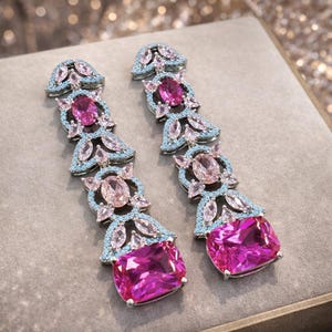 Puede incluir: Un par de pendientes largos colgantes con un engaste plateado. Los pendientes presentan una combinaci&oacute;n de piedras preciosas rosas y celeste claro. El dise&ntilde;o incluye piedras ovaladas y rectangulares, creando un accesorio glamuroso.
