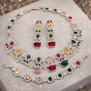 Puede incluir: Un deslumbrante conjunto de joyas que incluye collar, pendientes y pulsera. El conjunto est&aacute; adornado con una variedad de piedras preciosas de colores, incluyendo rojo, amarillo, verde, azul y rosa, engastadas en metal plateado. El dise&ntilde;o es intrincado y elegante.