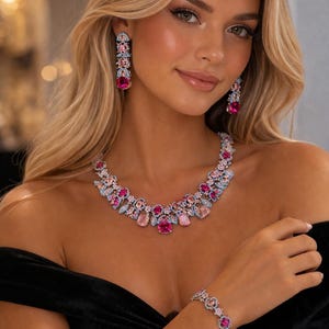Puede incluir: Un conjunto de joyas glamuroso que incluye collar, pendientes y pulsera. El conjunto presenta un dise&ntilde;o floral con piedras preciosas rosas y celeste. El collar y los pendientes son largos y elegantes, mientras que la pulsera es una cadena delicada.