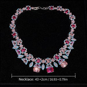 Puede incluir: Un collar brillante con piedras preciosas rosas, celeste y transparentes. El collar presenta un dise&ntilde;o floral con piedras de diversas formas y tama&ntilde;os. El collar mide 43 cm de largo. Sobre un fondo negro.