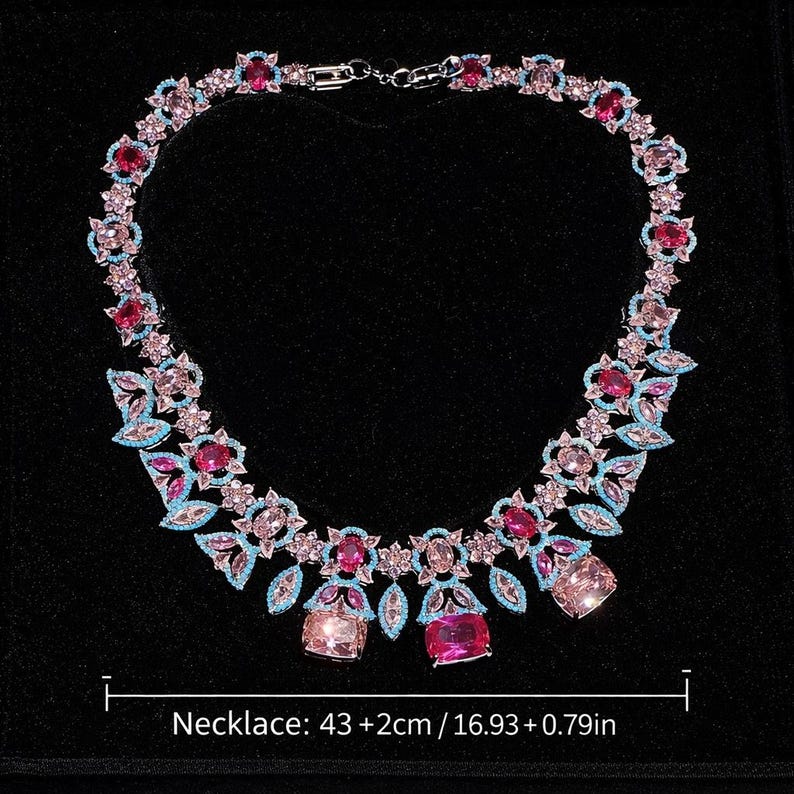 Puede incluir: Un collar brillante con piedras preciosas rosas, celeste y transparentes. El collar presenta un dise&ntilde;o floral con piedras de diversas formas y tama&ntilde;os. El collar mide 43 cm de largo. Sobre un fondo negro.