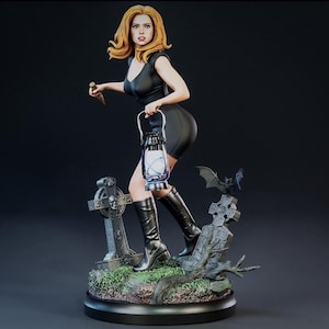 May include: A figurine of a woman in a black dress and boots, holding a lantern and a stake, set in a graveyard scene with tombstones and a bat. The figure has blonde hair and is in a running pose.