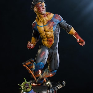 Puede incluir: Estatua detallada de un superhéroe en pose dinámica, con traje negro y amarillo y marcas de sangre. La figura está en el aire, con un alienígena derrotado en la base. Fondo oscuro.