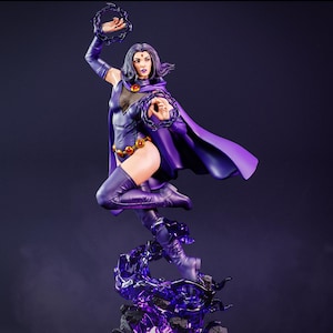 Op de afbeelding: Een gedetailleerd beeld van Raven, een DC Comics-personage, in een dynamische pose. Ze draagt een paars bodysuit, cape en laarzen, met een gouden riem. Raven is omgeven door paarse energie-effecten, met een donkere ring in elke hand. Donkerpaarse achtergrond.