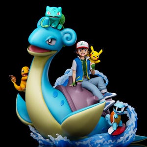 May include: A detailed figurine featuring characters from the Pokémon franchise. The central figure is a large, blue Lapras with a rider. Other Pokémon characters include Pikachu, Bulbasaur, Charmander, and Squirtle. The figurine is set against a black background.