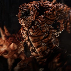May include: A detailed, brown monster figure with sharp teeth and red eyes. The figure has a textured, rough skin appearance and is posed in a dynamic stance. The image includes text that reads "PRESUPPORT READY 1-6 SCALE" and "AVAILABLE ON PATREON".