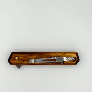 May include: A closed pocket knife with a wooden handle and a silver metal clip. The handle has a rich, brown wood grain pattern. The knife is set against a white background.