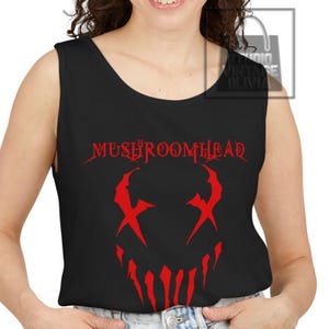 May include: A black sleeveless tank top featuring a red graphic print on the front. The design includes the text MUSHROOMHEAD in a stylized font above a red graphic of a jagged, sharp-toothed face with X-shaped eyes, centered on the chest.