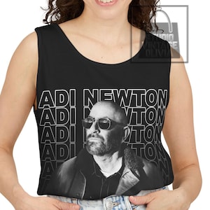 May include: A black sleeveless tank top featuring a repeating white outline text graphic that reads ADI NEWTON. Centered below the text is a black and white photographic print of a bearded person wearing dark sunglasses and a collared jacket.