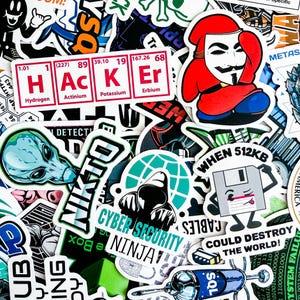 May include: A collection of colorful stickers with various designs. Notable stickers include a periodic table spelling "HACKER", an alien head, a Guy Fawkes mask, and a floppy disk with the text "WHEN 512KB COULD DESTROY THE WORLD!".
