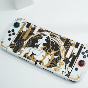 Può includere: Una console Nintendo Switch bianca con una skin personalizzata con un design nero e oro. La skin presenta un'illustrazione centrale e motivi geometrici. La console ha pulsanti di controllo blu e rossi.