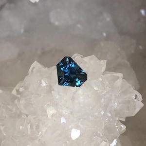 以下が含まれることがあります： 白い水晶の背景に置かれた、ファセットカットされた濃い青色の宝石