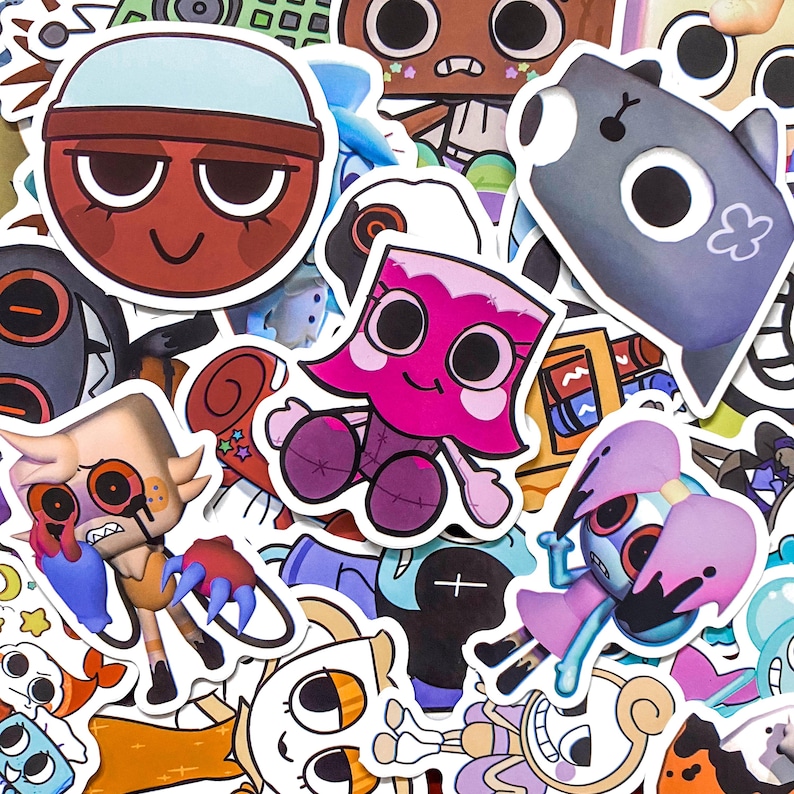May include: A collection of assorted vinyl stickers featuring various cartoon characters with large eyes, including a red circular face, a pink figure, a grey creature, and a tan character with red eyes, all arranged in a dense, overlapping collage.
