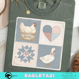 Puede incluir: Camiseta verde salvia con un gráfico cuadrado que presenta una gallina en un cuenco con la palabra "HOME", un corazón de retazos, una estrella y un pato con un lazo. La camiseta tiene una etiqueta Comfort Colors.