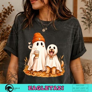 Puede incluir: Una camiseta gris carbón con un gráfico de un fantasma con gorro naranja que sostiene una taza de café con la palabra MEH, junto a un perro disfrazado de fantasma con pajarita, todo rodeado de hojas de otoño y tallos de trigo.