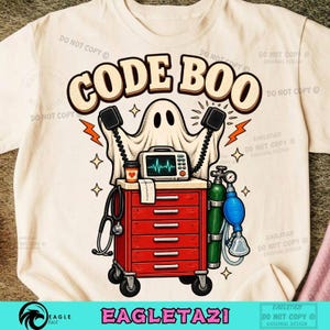 Puede incluir: Una camiseta de color crema con un gráfico de un fantasma sosteniendo paletas de desfibrilador sobre un carro médico rojo. El carro contiene un monitor cardíaco, una taza de café, un estetoscopio y un tanque de oxígeno. El texto CODE BOO está impreso en letras beige grandes y negritas.
