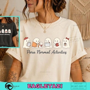 Peut inclure: Un t-shirt couleur crème arborant un motif de cinq fantômes blancs occupés à diverses activités, avec le texte Para Normal Activities imprimé en dessous. Les fantômes sont représentés avec des objets comme un presse-papier, une écharpe, un livre et une tasse de café.