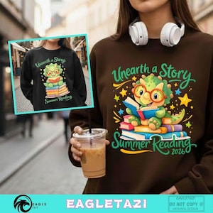 May include: A brown sweatshirt with a graphic of a cartoon dinosaur reading books, wearing glasses, and the text "Unearth a Story Summer Reading 2026". The design includes stars and colorful accents.