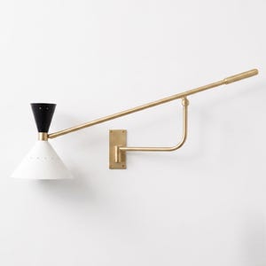 May include: A wall-mounted swing arm lamp featuring a long brass arm and a dual-tone conical shade. The upper portion of the shade is black, while the lower portion is white, both accented with small perforated holes along the edges.