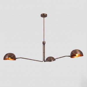 May include: A copper-toned metal chandelier featuring a central vertical rod and three adjustable horizontal arms, each ending in a semi-spherical dome shade. The interior of each dome is illuminated, casting a warm glow from the light source.