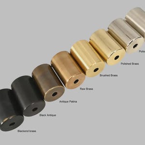 May include: A collection of seven cylindrical metal hardware knobs arranged in a diagonal line. The finishes include blackend brass, black antique, antique patina, raw brass, brushed brass, polished brass, polished chrome, and brushed chrome.