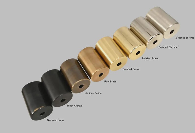 May include: A collection of seven cylindrical metal hardware knobs arranged in a diagonal line. The finishes include blackend brass, black antique, antique patina, raw brass, brushed brass, polished brass, polished chrome, and brushed chrome.