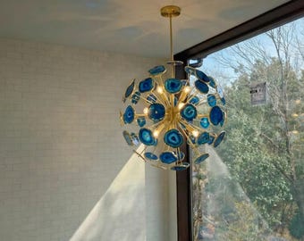 May include: A spherical chandelier featuring a gold-toned metal frame with numerous radiating arms. Each arm is tipped with a circular, polished blue agate slice. The fixture is illuminated, casting a warm glow from the center of the structure.