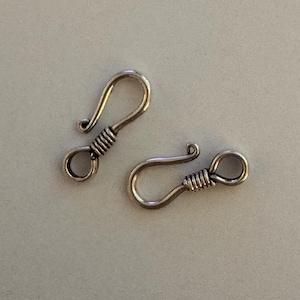 May include: Two silver-toned metal hook clasps, each featuring a circular loop at one end and a curved hook at the other. The center of each clasp is wrapped with a decorative wire coil, creating a textured appearance on the metallic surface.