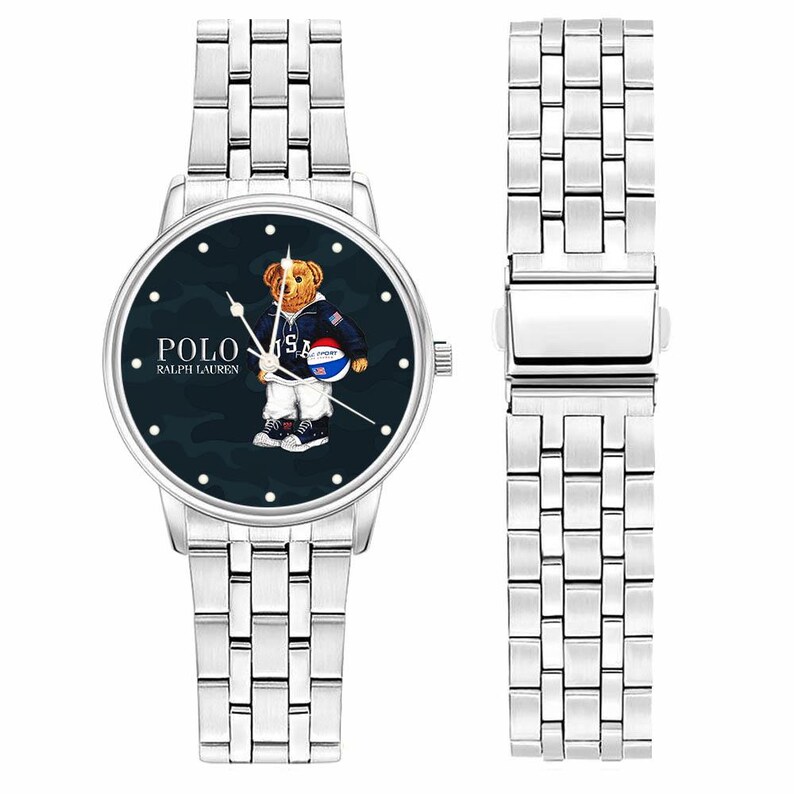 May include: Silver-toned wristwatch with a dark blue face featuring a bear wearing a jacket and holding a basketball. The watch face displays the text "POLO RALPH LAUREN". The watch has a silver band and a separate band piece.