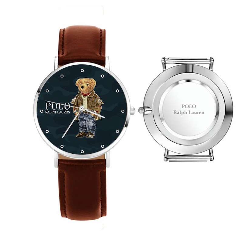 Op de afbeelding: Een Polo Ralph Lauren polshorloge met een bruine leren band. De wijzerplaat toont een beer in een jas en spijkerbroek, met het Polo-logo. De achterkant van het horloge is zilverkleurig met het Polo Ralph Lauren logo.