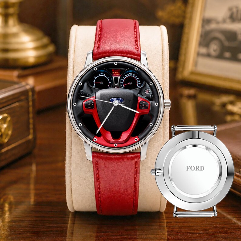 May include: A silver wristwatch with a red leather band. The watch face features a black background with a red and black steering wheel design. The word "FORD" is on the back of the watch.