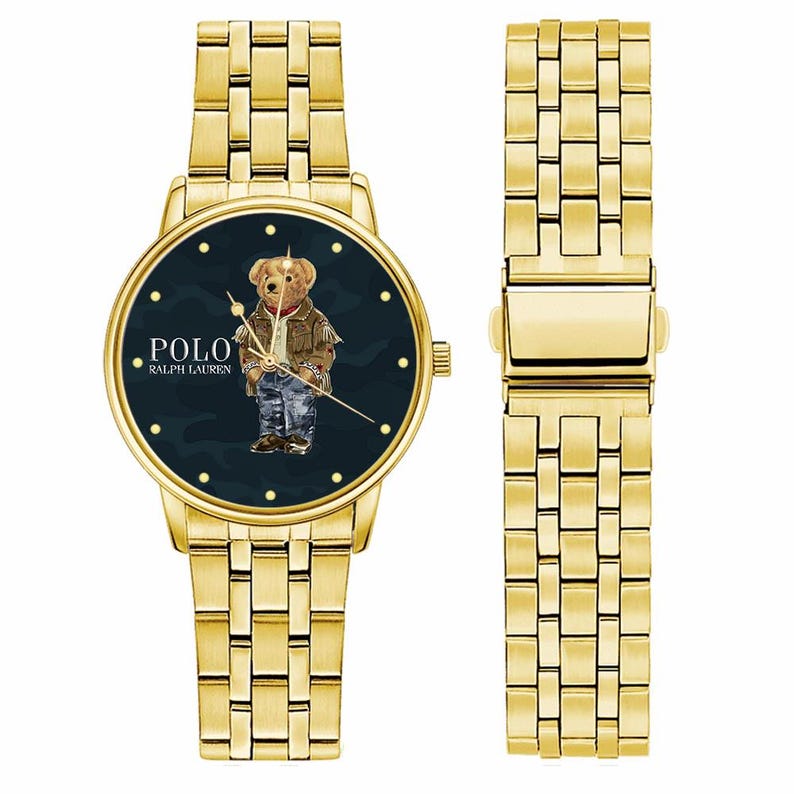 Op de afbeelding: Een goudkleurig polshorloge met een donkerblauwe wijzerplaat met een berenillustratie die een jas en jeans draagt. Het horloge heeft een bijpassende gouden band en de merknaam "POLO RALPH LAUREN" staat op de wijzerplaat.
