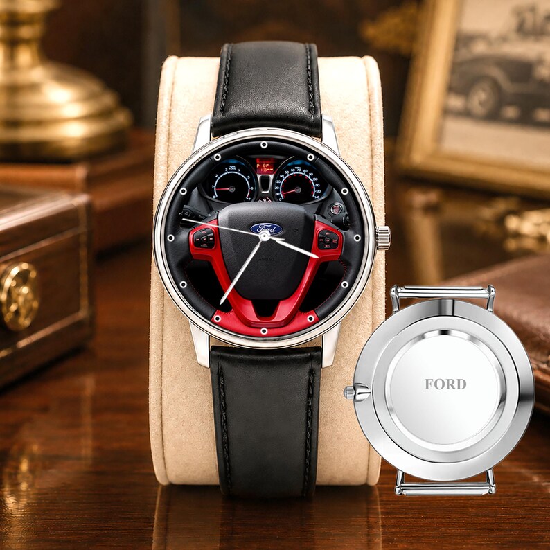 May include: A silver wristwatch with a black leather band. The watch face features a steering wheel design with red accents and the Ford logo. A separate watch back with the word "FORD" is also visible.