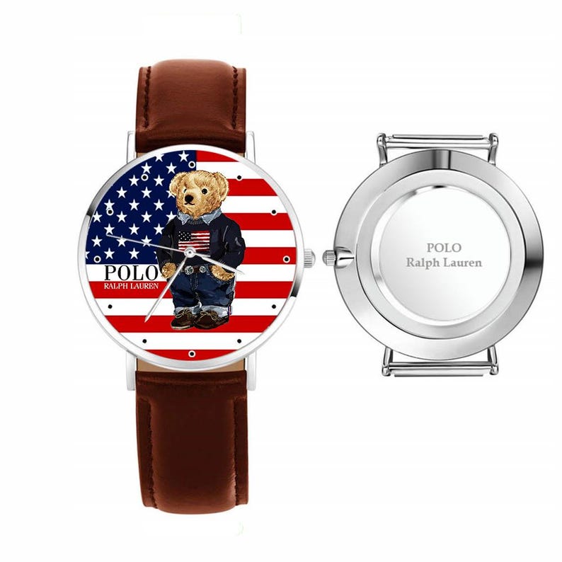 May include: A wristwatch with a brown leather band and a silver-colored case. The watch face features a bear wearing a jacket and jeans, set against a backdrop of the American flag. The brand name "POLO Ralph Lauren" is printed on the watch face.