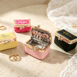 May include: Four small rectangular jewelry cases with gold-tone metal kiss-lock closures. One yellow case labeled Alaric, one pink polka-dot case labeled Darian, one black case labeled Alice, and one open pink case containing rings and a gray polka-dot lining.