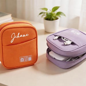 Peut inclure: Une trousse de rangement carrée orange avec le nom Jihane imprimé en écriture blanche et une trousse carrée violette contenant des câbles de charge blancs et une batterie externe, toutes deux avec des icônes électroniques blanches.