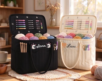 Könnte beinhalten: Zwei rechteckige Garnaufbewahrungstaschen, eine in Schwarz und eine in Creme, mit offenen Deckeln und elastischen Schlaufen für Häkelnadeln. Die schwarze Tasche ist mit dem Namen Anna und Schaf-Symbolen bestickt, die cremefarbene mit Laura.