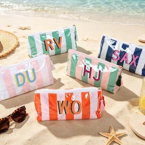 May include: Five rectangular zippered pouches with vertical stripes in various colors, each featuring two-letter monograms. The pouches are colored in green and white, navy and white, pink and white, green and pink, and orange and white, with matching tassels attached to the zippers.