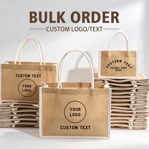 Op de afbeelding: Een collectie beige jute draagtassen met witte randen en hengsels. De tassen zijn voorzien van zwarte opdrukken met de tekst BULK ORDER, CUSTOM LOGO/TEXT, CUSTOM TEXT, YOUR LOGO en SECOND TEXT HERE. De tassen zijn in stapels gerangschikt.