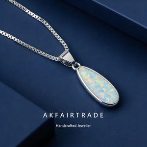 May include: A silver necklace with a teardrop-shaped opal pendant. The pendant has a white base with flashes of colour. The text "AKFAIRTRADE Handcrafted Jeweller" is below the necklace.