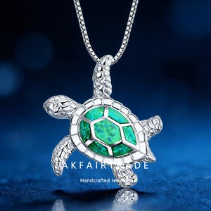Può includere: Collana con pendente a forma di tartaruga color argento con una gemma verde al centro. La collana ha una catena delicata e il testo "AKFAIRADE Handcrafted Jewels" è visibile.